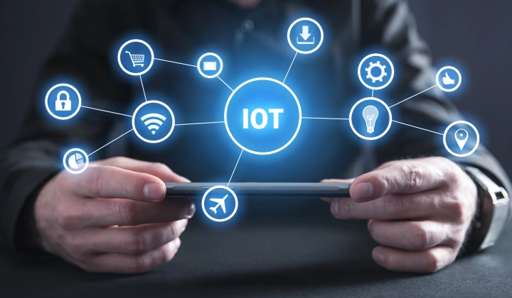 Hands holding a smartphone with a glowing IoT hub and connected device icons (lock, Wi‑Fi, car, light bulb) around it.